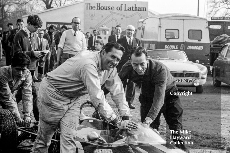 Driver Jack Brabham and designer Ron Tauranac push the Brabham Honda through the paddock at the Oulton Park Spring International meeting in 1965. The car was making its debut and Brabham offered to withdraw it from the race due to lack of speed (14mph slower on the straight than Graham Hill's Brabham BRM) but eventually it did start, lasting until lap 17.&nbsp;
