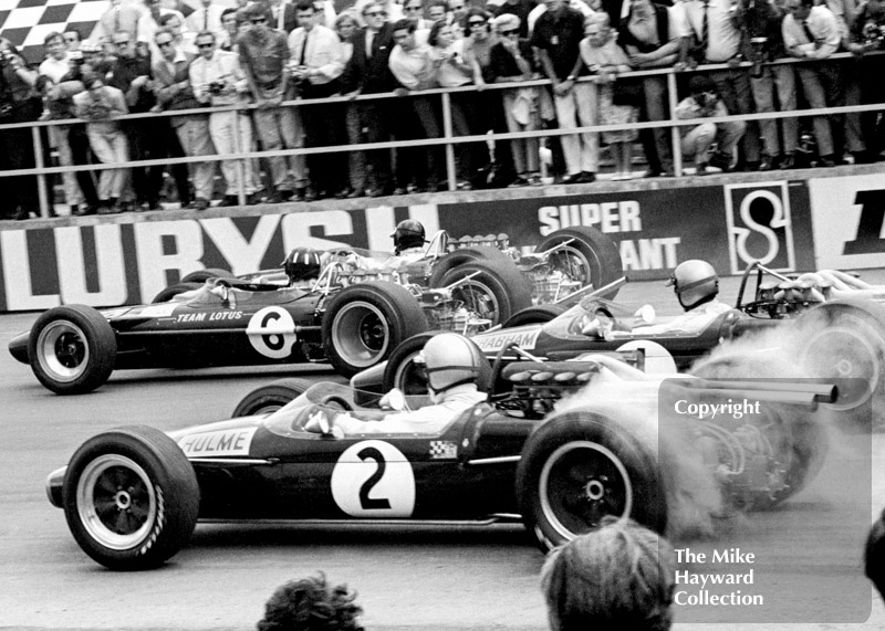 Jim Clark and Graham Hill, Lotus Cosworth 49s, and Jack Brabham and Denny Hulme, Repco Brabham BT24 V8s, leave the grid at Silverstone, 1967 British Grand Prix.
