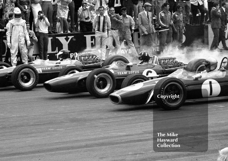 Jim Clark and Graham Hill, Lotus Cosworth 49s, and Jack Brabham, Repco Brabham BT24 V8, leave the grid at Silverstone, 1967 British Grand Prix.
