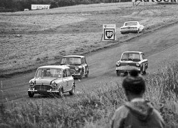 Edward Savory, Don Moore Mini Cooper S; Harry Ratcliffe, Vitafoam Mini Cooper S; and Mike Young, Superspeed Ford Anglia; Oulton Park, Gold Cup meeting 1964. Parked on the grass is the Ford Galaxie of Jack Sears, who retired with ignition failure.
